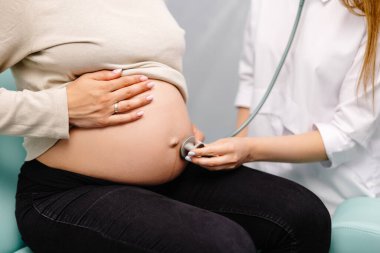 Steteskop kullanan kadın doktor klinikte hamile kadını muayene ediyor. Tıbbi muayene hamile kadın..