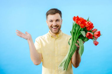 Elinde canlı kırmızı çiçeklerle ayakta duran bir adam..