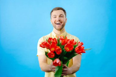 Elinde canlı kırmızı lale buketi tutan bir adam, tarafsız bir zemine karşı çiçeklerin güzelliğini sergiliyor..