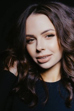 Siyah arka planda uzun kahverengi saçlı ve profesyonel makyajlı güzel bir kadın.