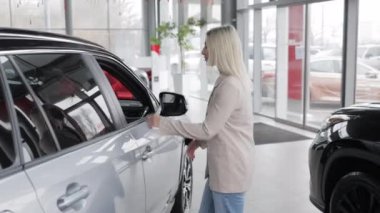 Satıcı kadın galeride yeni arabaya girmeye davet ediyor.