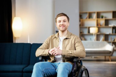 Olumlu yaşam tarzı, engelli kişi bakımı, rehabilitasyon ve evde destek. Genç beyaz adam tekerlekli sandalyede oturuyor, gülümsüyor ve oturma odasında kameraya bakıyor..