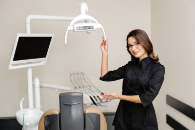 Modern klinikte genç bir dişçinin portresi. Bayan bir dişçi sizi nazikçe randevuya davet ediyor..