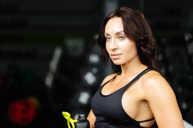 Spor yaptıktan sonra ayakta dinlenen ya da spor salonunda egzersiz yapan genç bir kadın. Spor salonundaki kadın dinleniyor ve spor kıyafetlerinde suyla rahatlıyor.