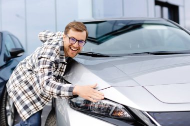 Galeride yeni arabasını kucaklayan sakallı genç adam neşeyle gülümsüyor..