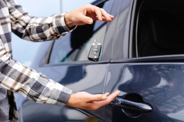 Duygusal adam elinde anahtarı tutuyor ve kameraya gülümsüyor. Yeni elektrikli arabasının anahtarını gösteren bir adam. Galeride araba alan genç bir adam..