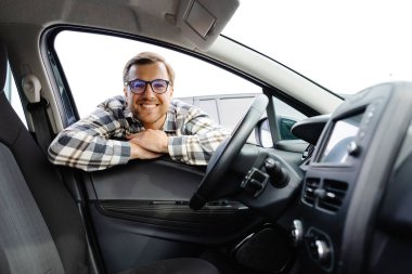 Genç adam yeni arabasının camından bakıyor, modern galeriden almadan önce kontrol ediyor. Galeride araba alan ya da kiralayan neşeli adam..