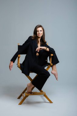 Yönetmen koltuğunda siyah takım elbise ve dantelli sutyen giymiş, saçına dokunan genç iş kadınının stüdyo portresi.