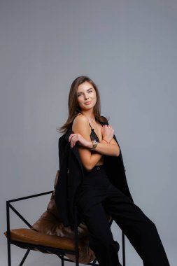 İş kadını ceketini çıkarırken gözleri kapalı, gri arka planı olan bir sandalyede oturuyor.