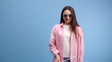 Gülümseyen mutlu genç kadın Amerikan bayrağı taşıyan günlük kıyafetler giyiyor ve mavi arka planda izole edilmiş kameraya bakıyor.