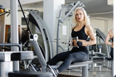 Güçlü bayan sporcu spor salonunda kablo yayını kullanarak sırt kaslarını çalıştırıyor. Sağlıklı yaşam tarzına olan bağlılığını ve gücünü gösteriyor.