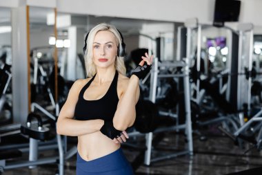 Genç sporcu kadın spor salonunda spor yaparken müziğin keyfini çıkarıyor. Spor kıyafetleriyle enerji ve motivasyon saçıyor.