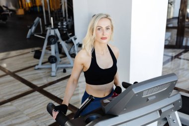 Modern bir spor salonunda koşu bandında kardiyo eğitimi alan atletik bir kadın, spor ve sağlıklı yaşama bağlılığını gösteriyor.