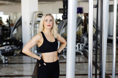 Spor salonundaki antrenman aletlerinin yanında kendinden emin duran genç sporcu, vücut bulmuş ve spor yolculuğuna kendini adamış.