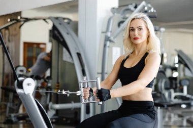 Güçlü bayan sporcu spor salonunda kablo yayını kullanarak sırt kaslarını çalıştırıyor. Sağlıklı yaşam tarzına olan bağlılığını ve gücünü gösteriyor.