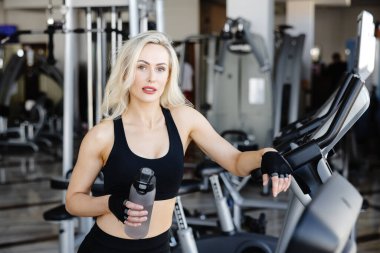 Spor salonundaki yoğun egzersizden sonra ferahlatıcı bir su içen genç sporcu kadın sağlıklı ve aktif bir yaşam tarzını benimsiyor.