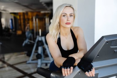 Modern bir spor salonunda koşu bandında kardiyo eğitimi alan atletik bir kadın, spor ve sağlıklı yaşama bağlılığını gösteriyor.