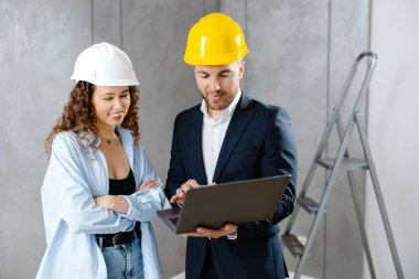 Çekici genç bayan müteahhit kasklı müşteriyle konuşuyor ve oturma odasında dizüstü bilgisayarla onarım sekansı gösteriyor. Ev sahibinin mühendis ya da mimarla görüşmesi