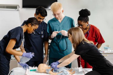 Bir bebek manken üzerinde entübasyon uygulayan çeşitli tıp öğrencileri grubu, simüle edilmiş bir tıbbi ortamda gerekli becerileri gösteriyorlar.