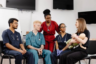 Çeşitli tıp öğrencileri, bir sınıftaki eğitim sırasında tıbbi bir manikinde bebek suni teneffüs yapıyor.