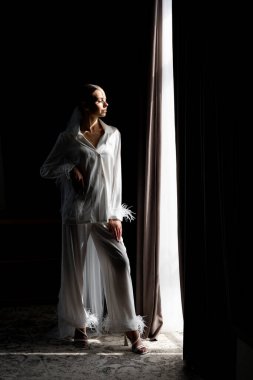 Gelin beyaz ipek pijama giyip, tüylü kelepçelerle düğün günü iki siyah perde arasında perde açıyor.