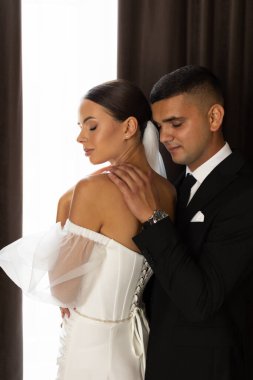 Yeni evliler arasında romantik bir an, damat gelinin omzuna hafifçe dokunuyor, düğün günlerinde sevgi ve yakınlığı ifade ediyor.