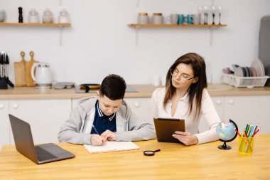 Genç bir kadın bir çocuğa tablet ve küre kullanarak derslerinde yardım ediyor. Evde eğitim gören bir öğrenci ödevini özel öğretmenin yardımıyla yapar..