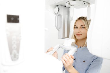 Modern bir diş kliniğinde diş panoramik radyografi sınavına giren hasta gülümsüyor.