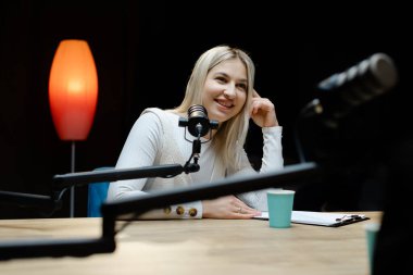 İçerik yaratıcısı, rahat bir ev stüdyosunda ses podcast 'i kaydederken bir mikrofonla meşgul oluyor, mutluluk ve yaratıcılık yayıyor.