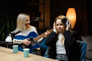 İki bayan müzisyen bir stüdyoda akustik gitar ve profesyonel mikrofonla şarkı çalıyor ve kaydediyor.