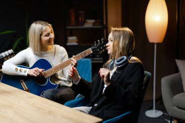 Bir şarkı besteleyen iki bayan müzisyen, biri akustik gitar çalıyor diğeri de kayıt stüdyosunda zaman tutuyor.