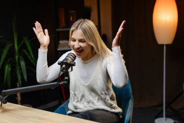 Kadın podcaster, profesyonel ekipmanlar ve canlı bir atmosferle çevrili modern bir stüdyoda gösterisini kaydederken hareketli bir şekilde hareket ediyor.