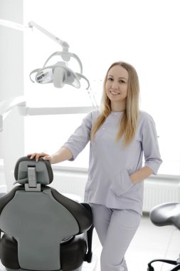 Modern ve parlak diş muayenehanesinde gülümseyen dişçi kadın, ekipmanların yanında duruyor.