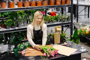 Çiçekçide pembe lale buketi düzenleyen, kahverengi kağıtla saran, teslimat ya da müşteri alımına hazırlanan bir çiçekçi.