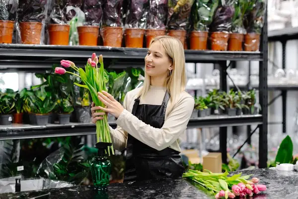 Renkli bitkiler ve güzel çiçeklerle çevrili büyüleyici bir çiçekçide canlı pembe laleler düzenleyen bir çiçekçi.