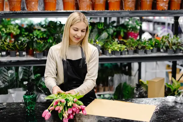 Çiçekçi elinde pembe lalelerden oluşan canlı bir buket tutuyor, büyüleyici bir çiçekçide çiçeklerle çevrili, çiçekçiye neşe ve tutku saçıyor.