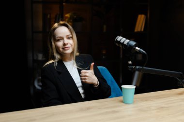 İçerik yaratıcısı, rahat bir ev stüdyosunda ses podcast 'i kaydederken bir mikrofonla meşgul oluyor, mutluluk ve yaratıcılık yayıyor.