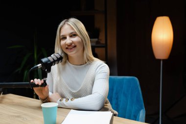 İçerik yaratıcısı, rahat bir ev stüdyosunda ses podcast 'i kaydederken bir mikrofonla meşgul oluyor, mutluluk ve yaratıcılık yayıyor.