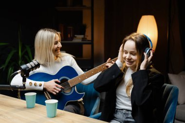 İki bayan müzisyen bir stüdyoda akustik gitar ve profesyonel mikrofonla şarkı çalıyor ve kaydediyor.