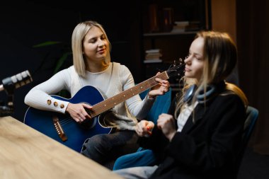 Bir şarkı besteleyen iki bayan müzisyen, biri akustik gitar çalıyor diğeri de kayıt stüdyosunda zaman tutuyor.