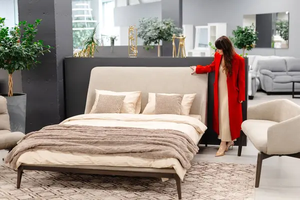 Müşteri şık bir bej çift yatak seçiyor. Mobilya mağazasının vitrininde. Yumuşak yatak ve rahat yastıkları hissediyor.