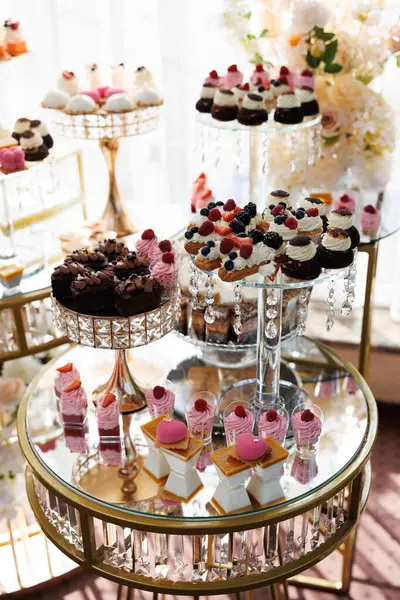 Çeşitli hamur işleri ve pastalar taze böğürtlenlerle süslenmiş cam ve altın katlı sergiler düğün resepsiyonunda