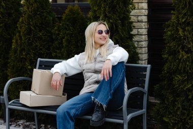 Modern evinin dışındaki bankta dinlenen şık bir kadın yanında paketler, huzur dolu bir anın tadını çıkarıyor.