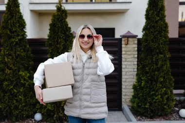 Gülümseyen teslimatçı kadın evin önünde iki karton kutu taşıyor, teslimat ve nakliye endüstrisi konsepti