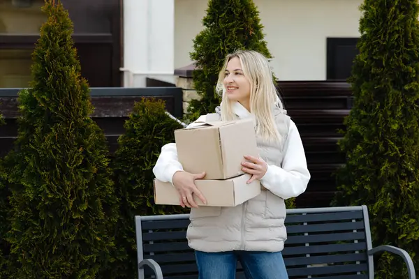 Mutlu müşteri online sipariş alıyor, gülümsüyor ve evinin önündeki bankın yanında karton kutular tutuyor.