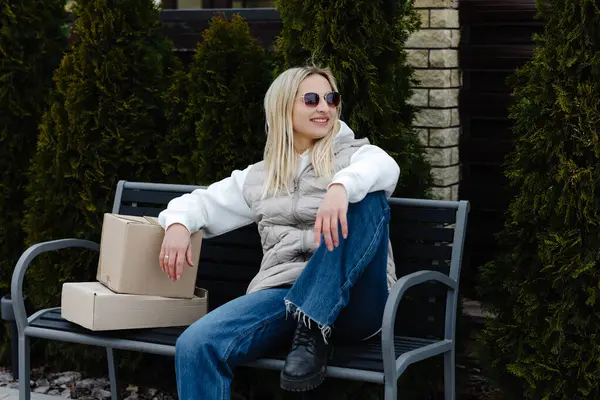 Modern evinin dışındaki bankta dinlenen şık bir kadın yanında paketler, huzur dolu bir anın tadını çıkarıyor.