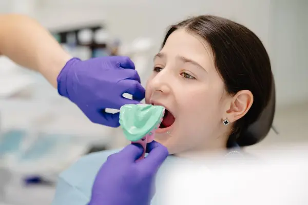 Diş hekimi mor eldiven takıyor. Ağız sağlığı için klinikteki genç bir kızın ağzına diş izi tepsisi yerleştiriyor.