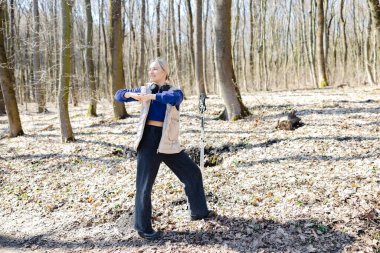 Genç sporcu, kulaklıklar ve direklerle yürüme eğitimi sırasında ormanda kollarını uzatıyor.