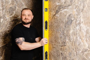 İnşaatçı, bir duvar yenileme çalışmaları sırasında hassasiyet ve doğruluğu sağlamak için, bir seviye aracı ile mermer fayansların eşitliğini kontrol ediyor