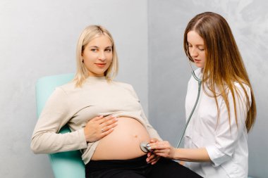 Steteskop kullanan kadın doktor klinikte hamile kadını muayene ediyor. Tıbbi muayene hamile kadın..